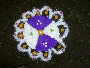Farverig Rangoli lavet af rispulver og blomsterblade på jorden.