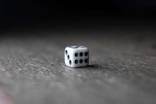 A focused close-up of a white dice with black dots placed on a textured wooden surface.