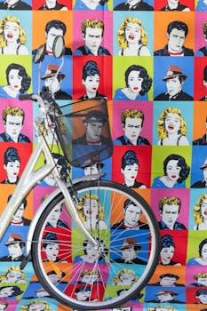 Bicycle with basket positioned in front of a vibrant pop art background featuring iconic figures.